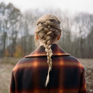 Taylor Swift evermore era with long blonde braid and rustic plaid coat in winter forest